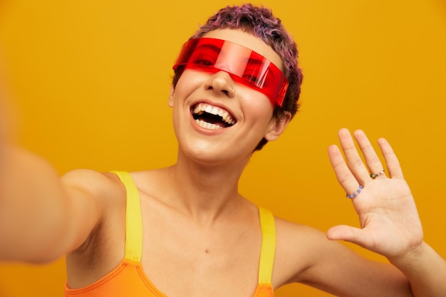 Woman wearing unusual millennial glasses taking selfies in sportswear against an orange studio background free space