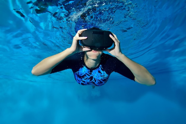 A woman wearing virtual reality glasses on her head is swimming and posing underwater in the pool