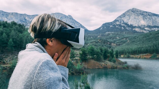 Foto donna che indossa un simulatore di realtà virtuale contro montagne e cielo