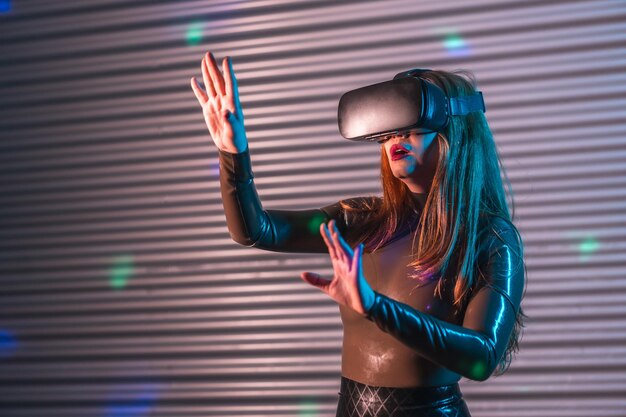 Photo woman wearing a vr goggles and gesturing raising arms in an futuristic night space with neon lights