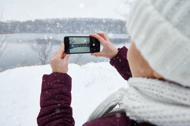 A woman wearing warm clothes holding smartphone and making a shoot of naturview mode.