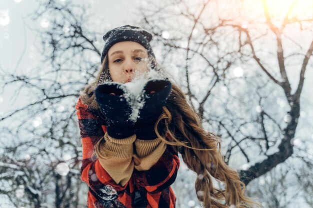 暖かい冬の服と帽子をかぶった女性冬の公園で雪を吹き飛ばし雪花を飛ばす晴れた日