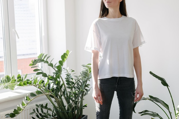 あなたのロゴ、モックアップ、または屋内でデザインするためのスペースのある白い空白のTシャツを着ている女性