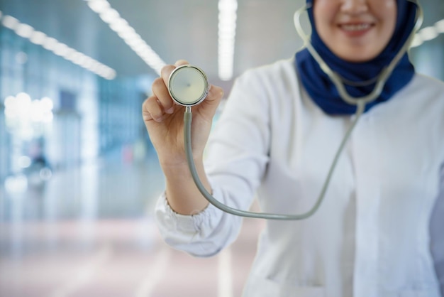 A woman wearing a white coat holds a stethoscope in her hand.