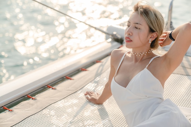 Woman wearing white dress relax on sailing yacht, romantic sunset