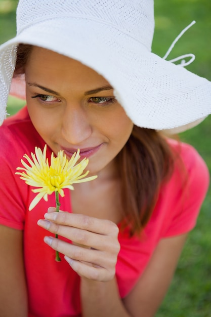 白い帽子を身に着けている女性が側を見ながら花を嗅ぐ