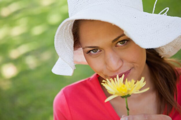 白い帽子を身に着けている女性は、黄色の花を嗅ぐ