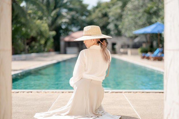 Woman wearing white shirt long skirt and straw hat posing near swimming pool
