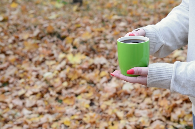 緑のコーヒーカップを保持している白いセーターを着ている女性