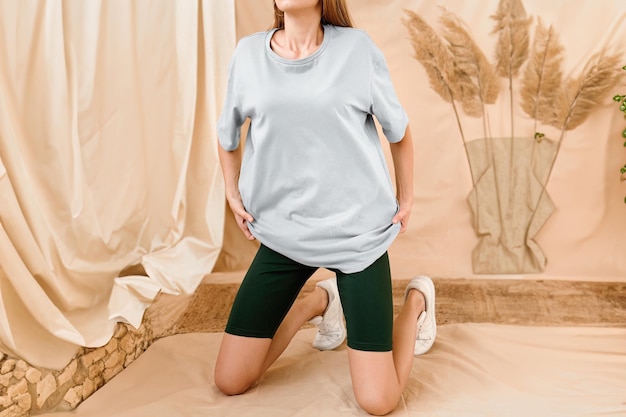 한 여성이 스튜디오에서 큰 크기의 셔츠를 입고 있습니다. 스트리트웨어 의상 젊은 소녀는 텍스트와 로고 배치를 위한 셔츠 디자인의 고립된 모형입니다.