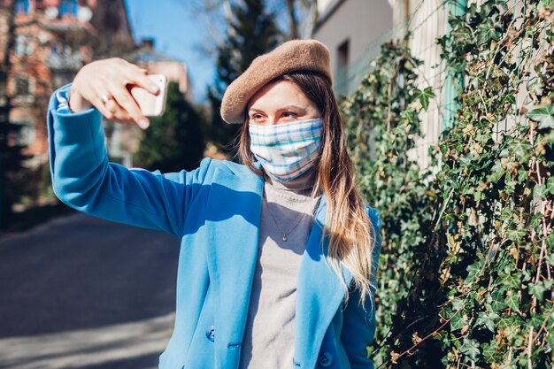 Photo woman wears reusable mask outdoors during coronavirus covid-19 pandemic. girl taking selfie on empty street