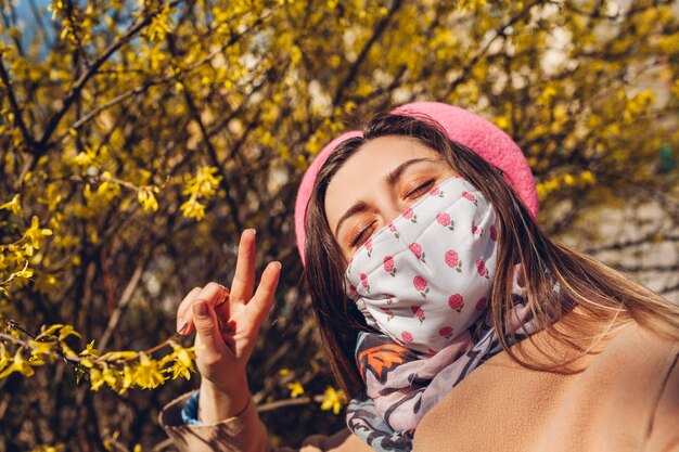 Photo woman wears reusable mask outdoors during coronavirus covid-19 pandemic. woman takes selfie with flowers. stay safe