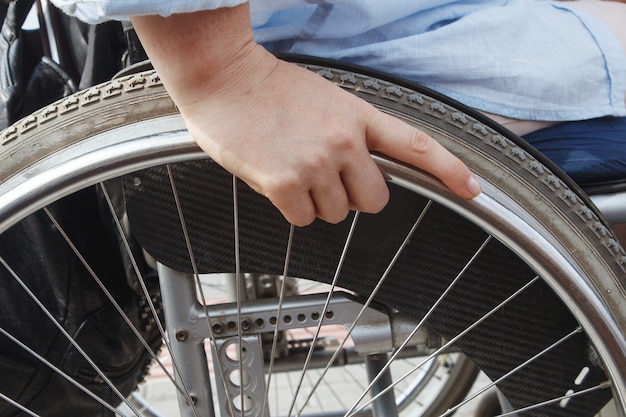 Woman in a wheelchair in the city park. The concept of an accessible environment for disabled people. Close up of hand and while.