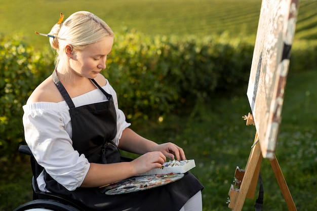 Donna in sedia a rotelle pittura all'aperto nella natura