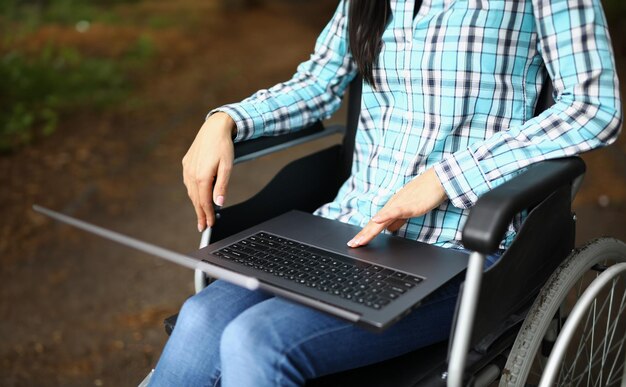 Foto donna in sedia a rotelle nel parco con il portatile in grembo primo piano lavoro a distanza freelance e formazione per disabili