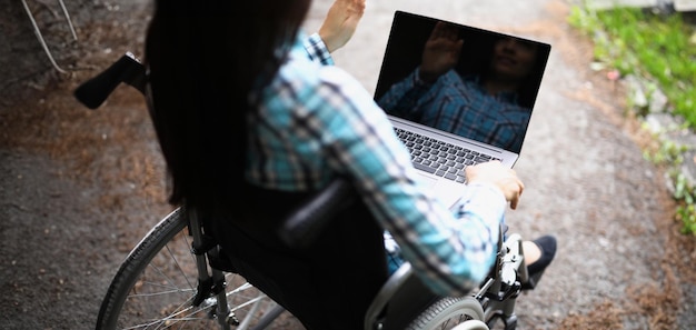 Woman in wheelchair wave hello on video call laptop for remote work