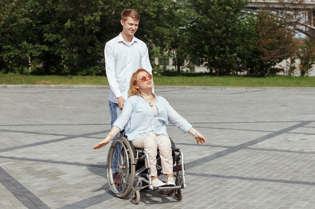 Woman in a wheelchair with her boyfriend strolling in the city summer park.