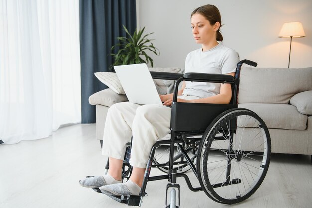 車椅子の女性は、補助犬を連れてホームオフィスのラップトップPCで作業します。