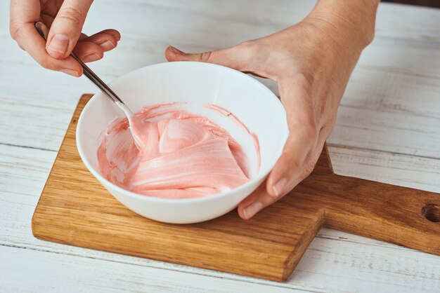 Woman whisking red cream for decorating cookies in bowl on kitchen, closeup