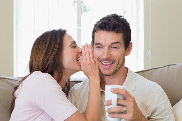 Woman whispering secret into a happy mans ear in living room