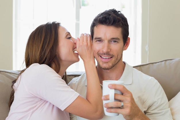 Woman whispering secret into a happy mans ear in living room