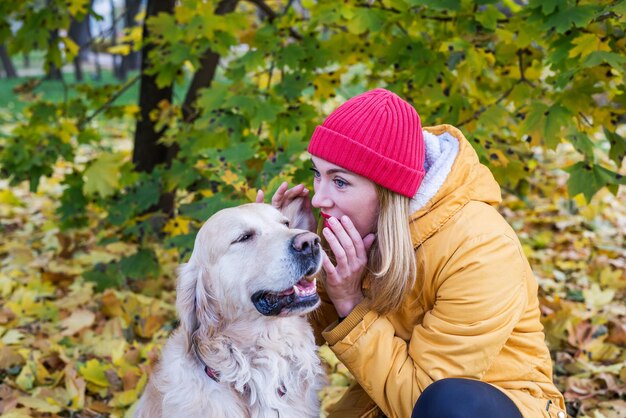 Una donna sussurra qualcosa all'orecchio del suo cane da riporto in un parco autunnale tra foglie gialle.