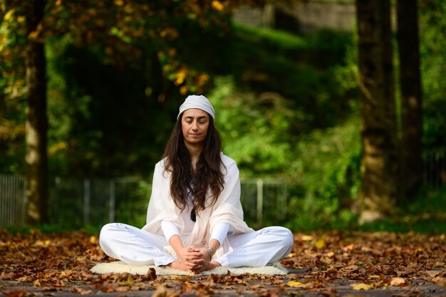 Woman in white in autumn park while doing yoga