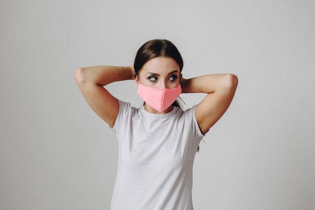 Woman on white background is standing in protective mask girl straightens her hair looking to side