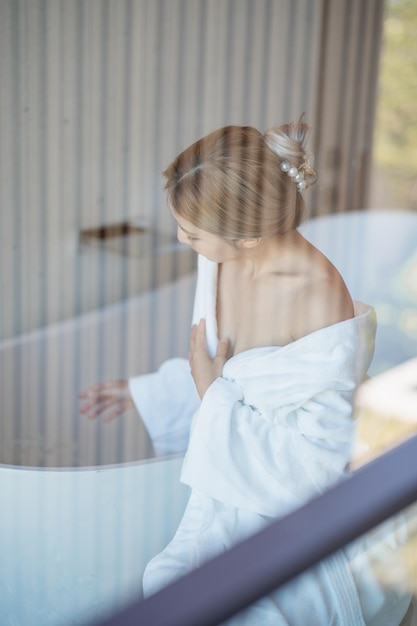 Woman in white bathrobe sitting on bathtub