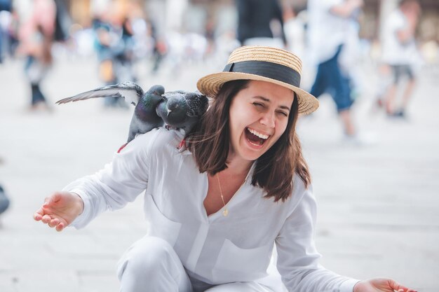 Woman in white clothes with straw hat having fun with pigeons at venice city square piazza san marco