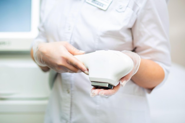 A woman in a white coat holds a laser hair removal machine in her hands