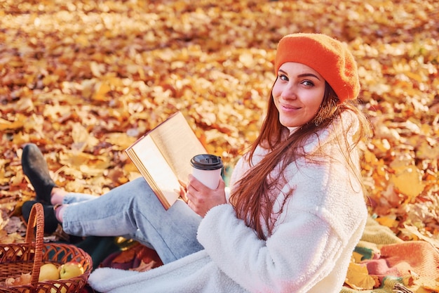 흰 코트를 입은 여자가 가을 공원에 앉아 있다