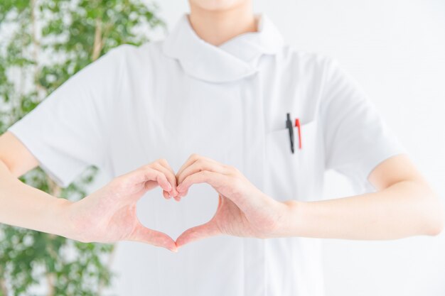 Woman in white coat making heart with hands