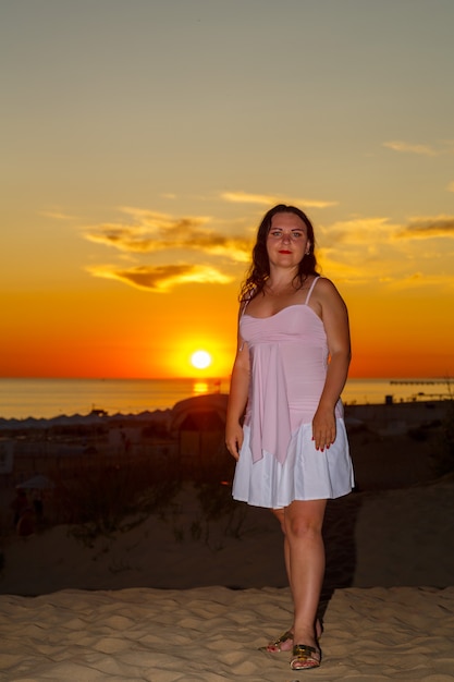 Donna in abito bianco sulla spiaggia sullo sfondo del mare al tramonto.