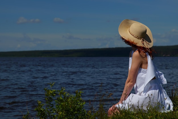 Woman in white dress and hat relax on riverside