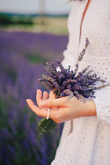 ラベンダーの花の花束を保持している白いドレスの女性がクローズアップ