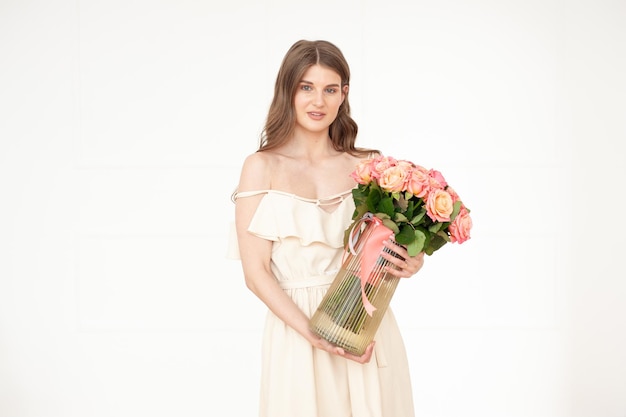 A woman in a white dress holds a vase of pink roses.