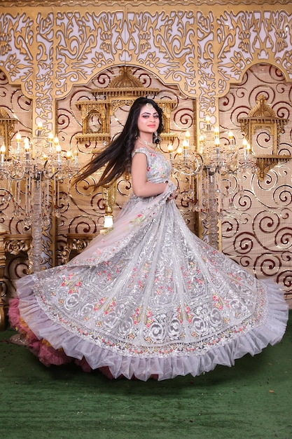 A woman in a white dress is posing in front of a gold wallpaper.