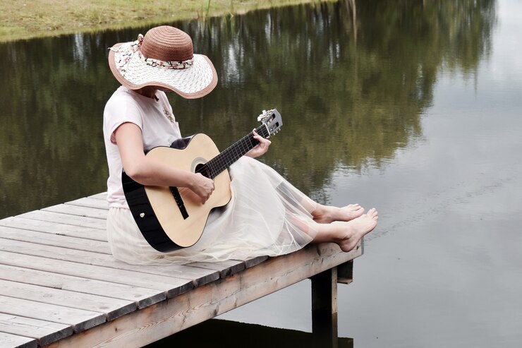 Photo woman in a white dress on a pier with a guitar