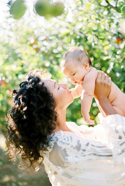 Woman in a white dress raises a baby in her arms in the garden