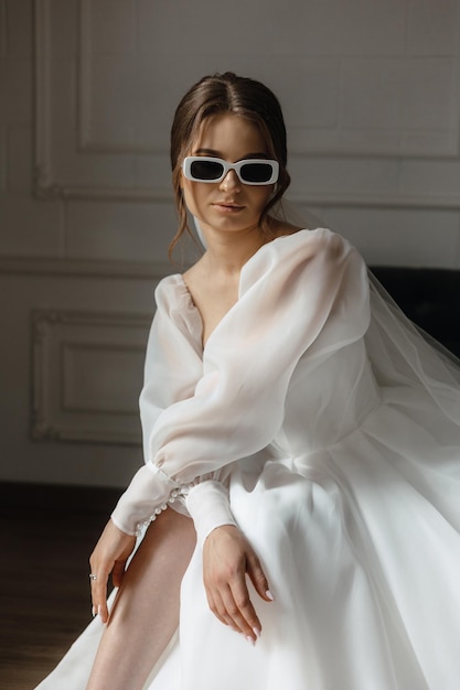 A woman in a white dress sits on a chair wearing sunglasses