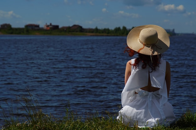 Woman in white dress sits on riverside, back view