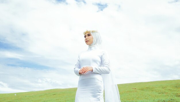 A woman in a white dress stands in a field with the sky behind her.