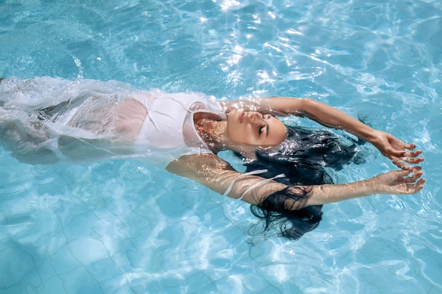 Woman in a white dress swims underwater in a pool