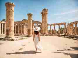 Photo a woman in a white dress walking amidst ancient ruins with tall columns and stone structures