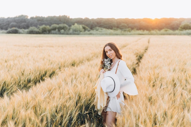 Donna con un vestito bianco e un cappello bianco in un campo di grano