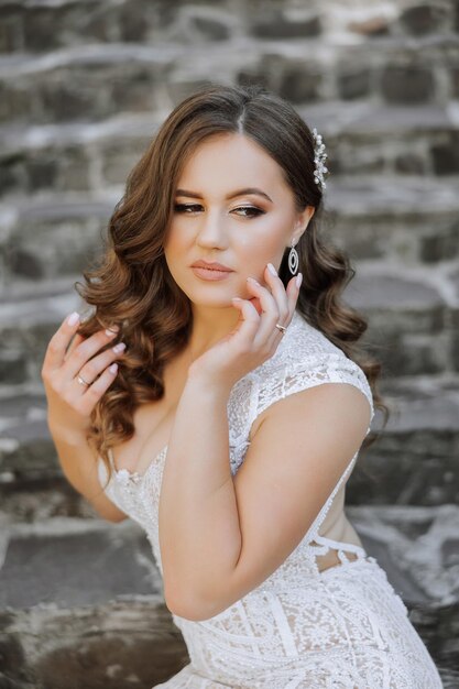 A woman in a white dress with long hair and earrings is posing for a photo