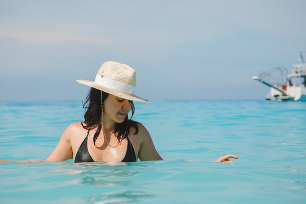 Woman in white hat and black swimsuit in blue sea water summer vacation