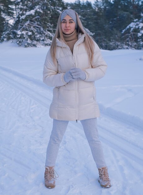 白いジャケットと帽子をかぶった女性が雪の中に立っています