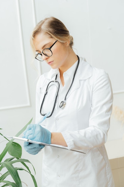 A woman in a white lab coat writes on a clipboard.